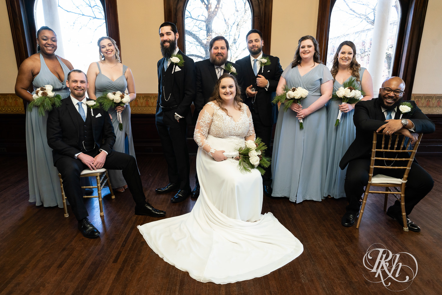 Wedding party in black suits and blue dresses smiling at Semple Mansion in Minneapolis, Minnesota.