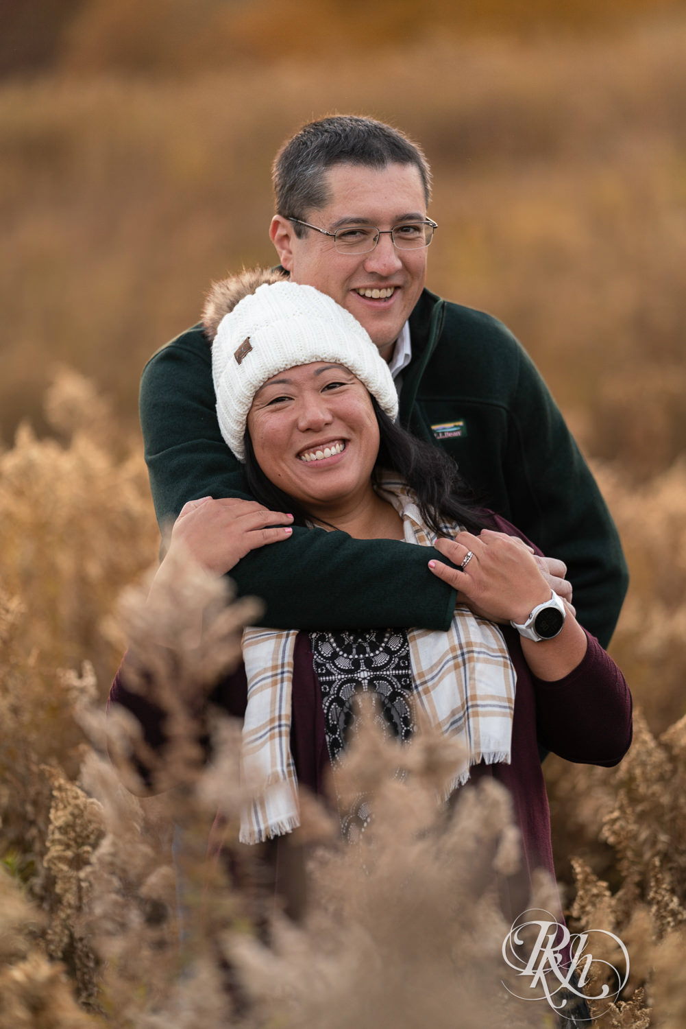 Man and Korean woman hug and laugh in field in fall colors at Lebanon Hills Regional Park in Eagan, Minnesota.