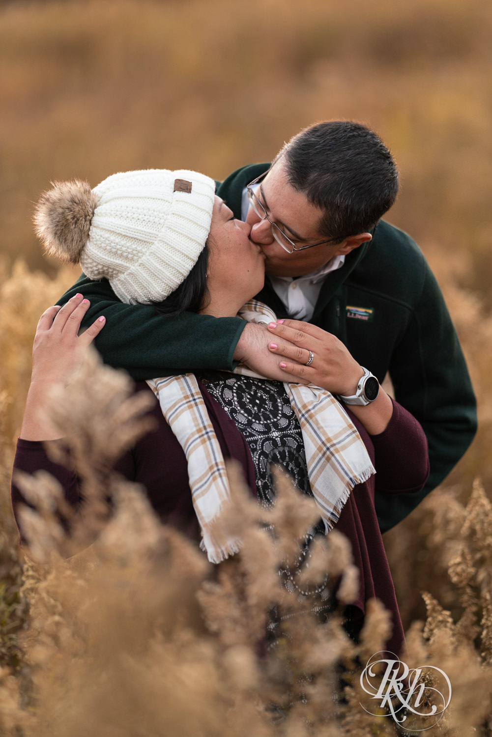 Man and Korean woman hug and kiss in field in fall colors at Lebanon Hills Regional Park in Eagan, Minnesota.