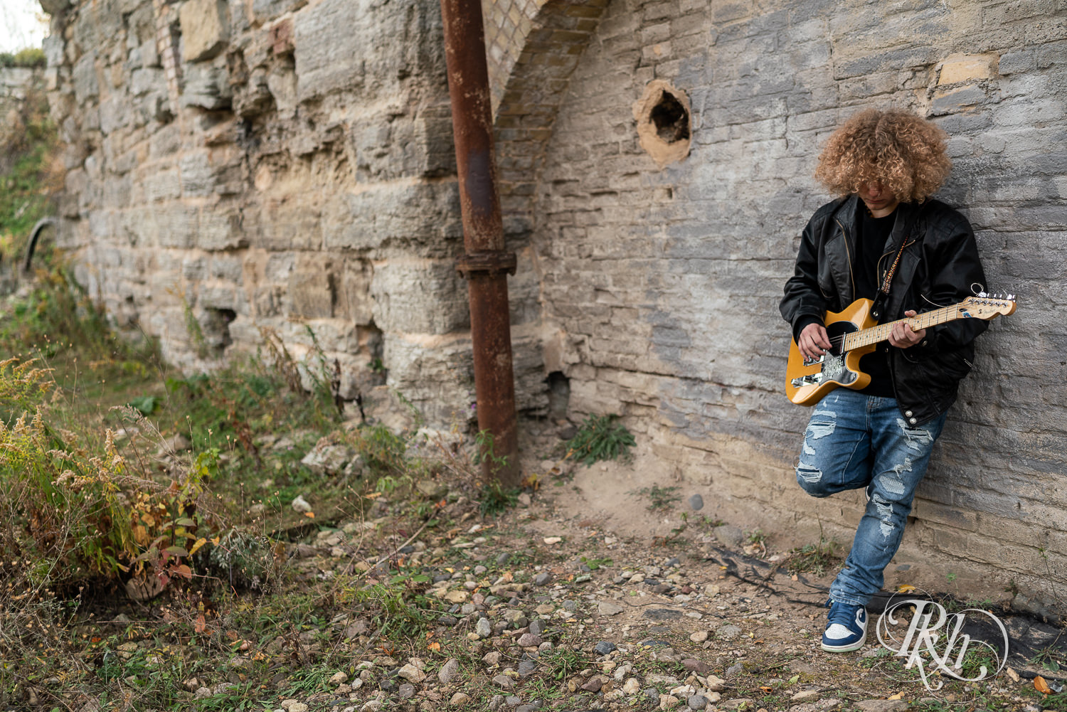 Senior boy playing dressed in leather and jeans plays guitar in downtown Minneapolis senior photography session.
