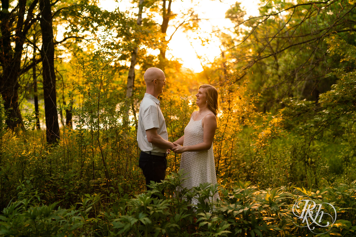 Man in white shirt and blonde woman in white dress and denim smile at sunset in Lebanon Hills Regional Park in Eagan, Minnesota.