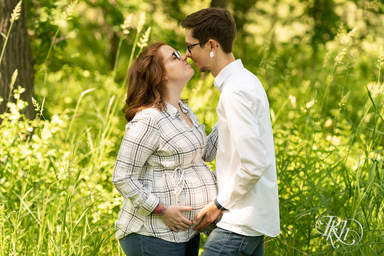 Pregnant woman holds belly with husband at Lebanon Hills Regional Park in Eagan, Minnesota during maternity photography session.