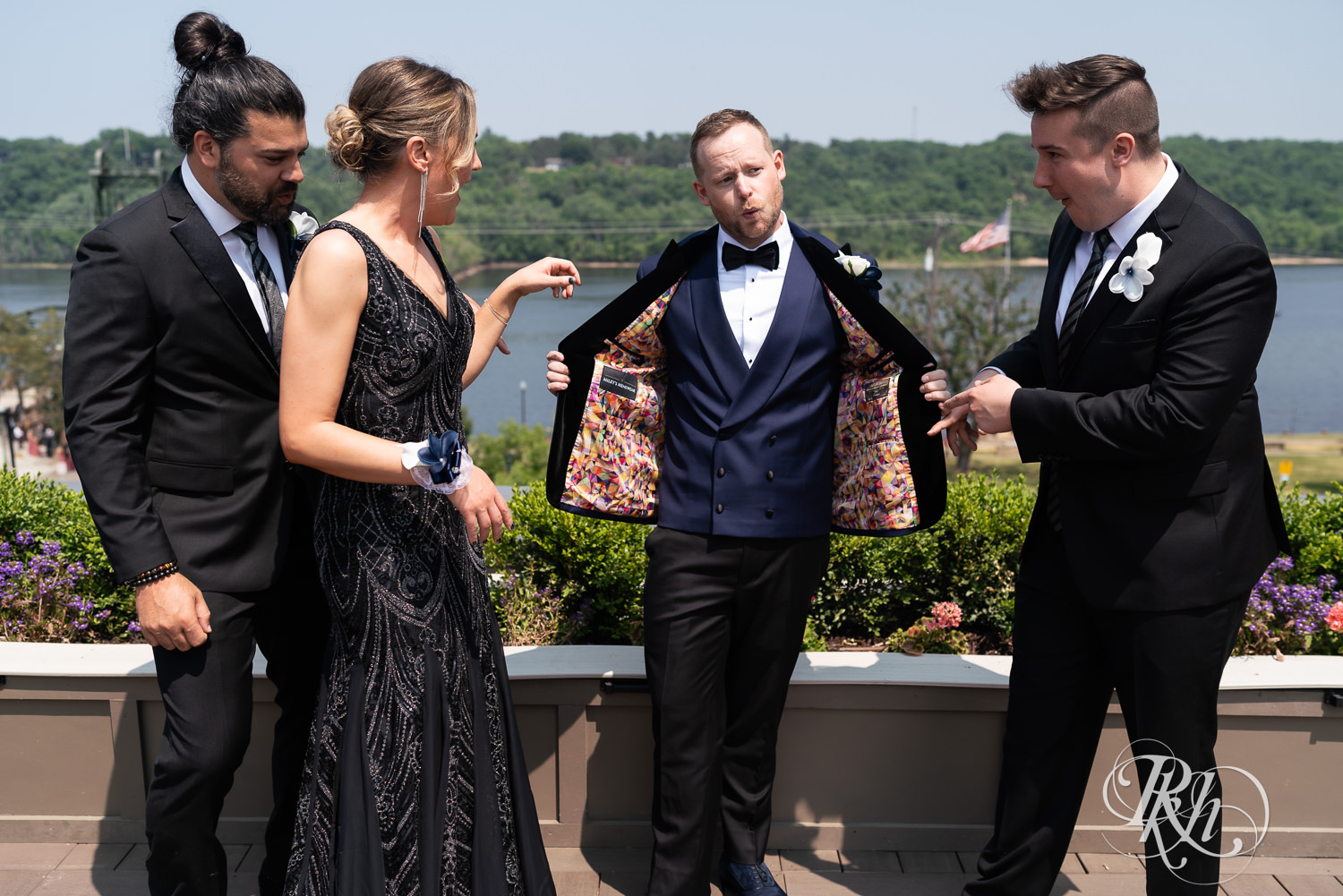 Grooms in blue tuxedos laugh on rooftop with wedding party before gay wedding in Stillwater, Minnesota.