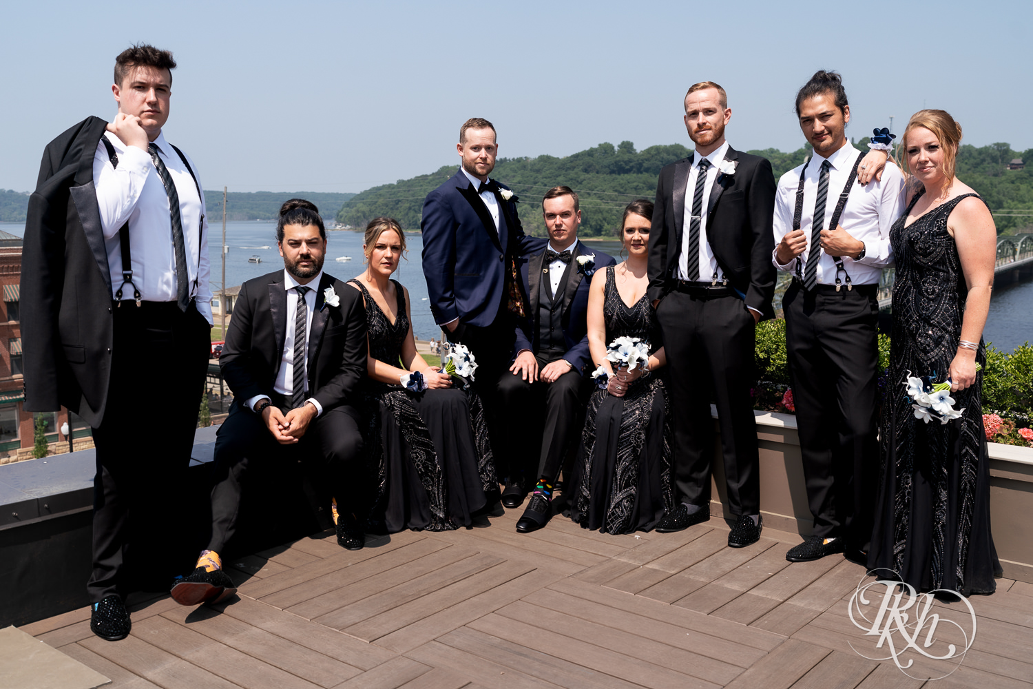 Grooms in blue tuxedos pose stoically on rooftop with wedding party before gay wedding in Stillwater, Minnesota.