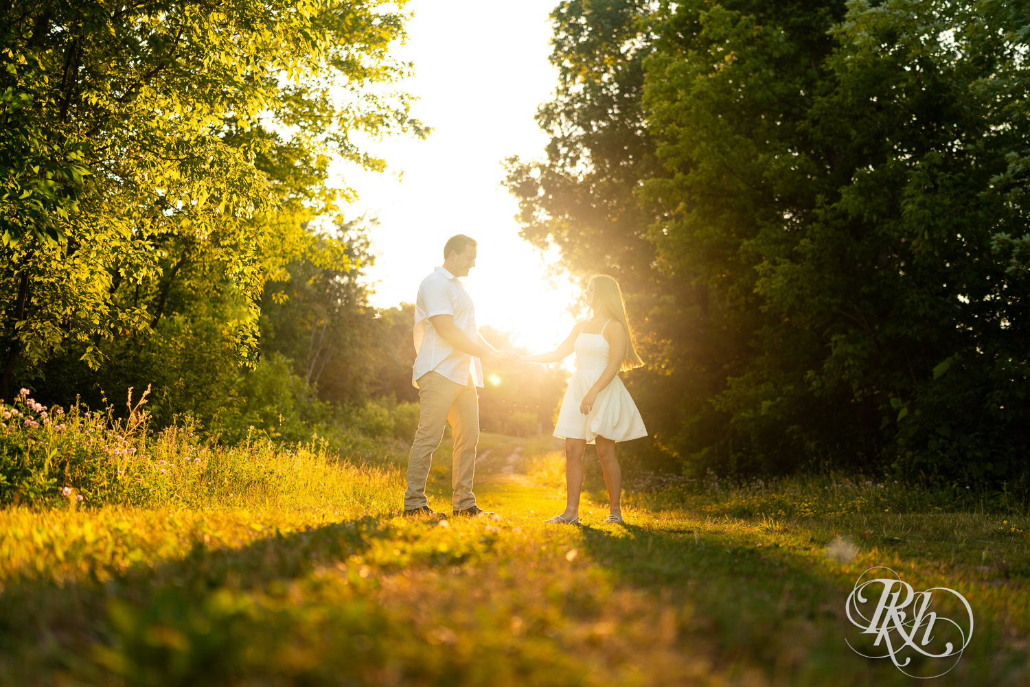 Man in white shirt and woman in white dress dance during golden hour engagement photography at Lebanon Hills in Eagan, Minnesota.
