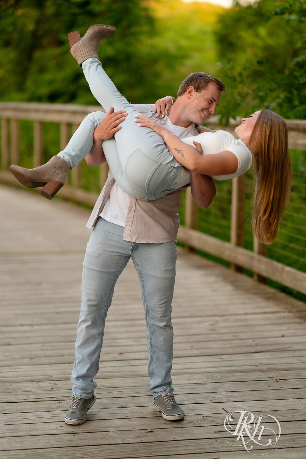 Man and woman in jeans laugh on bridge during golden hour engagement photography in Eagan, Minnesota.