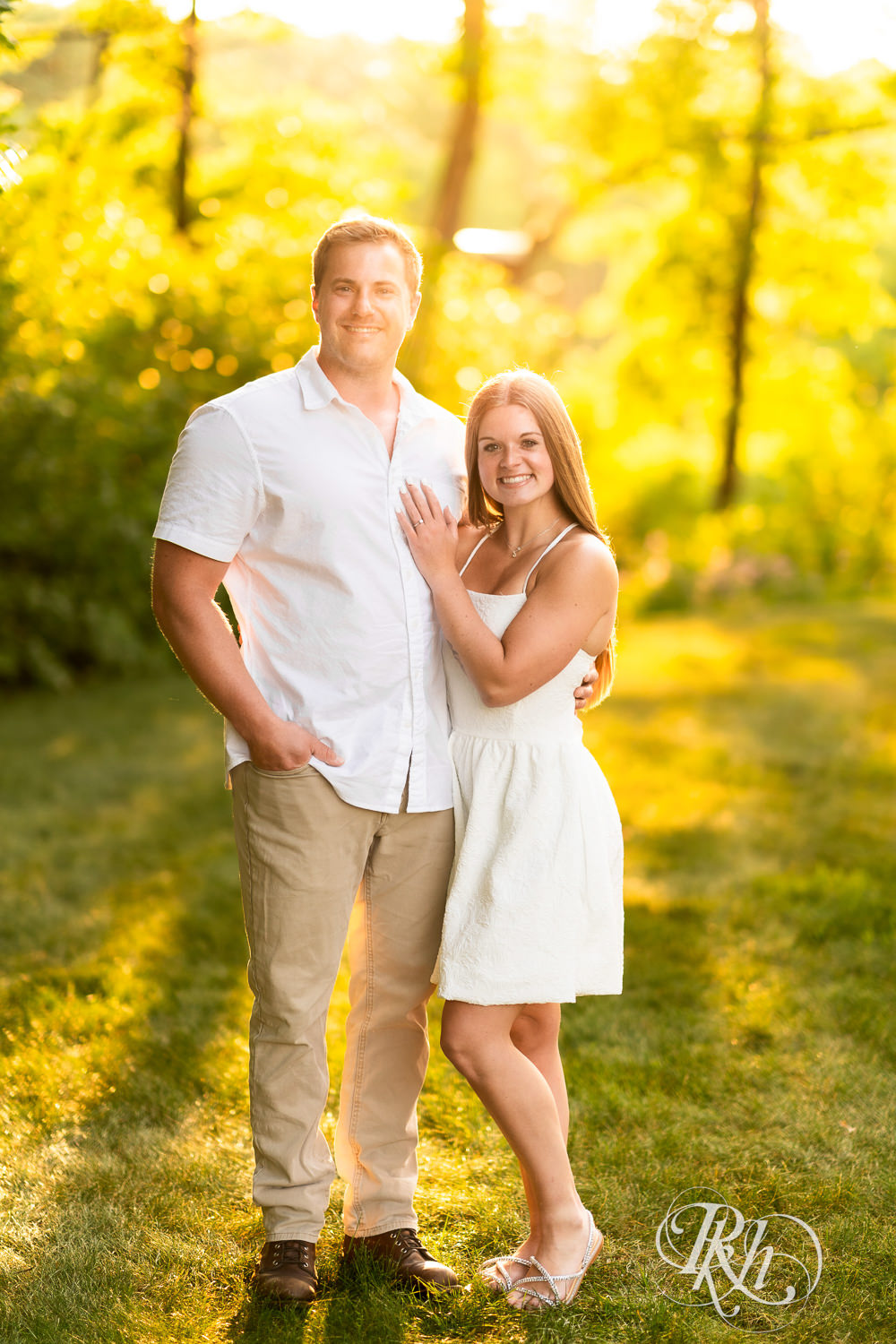 Man in white shirt and woman in white dress smile during golden hour engagement photography at Lebanon Hills in Eagan, Minnesota.