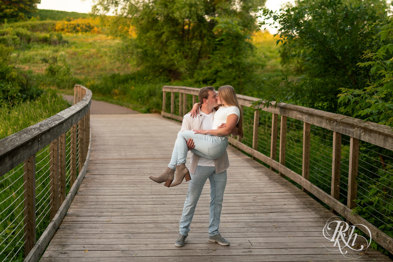 Man and woman in jeans kiss on bridge during golden hour engagement photography in Eagan, Minnesota.