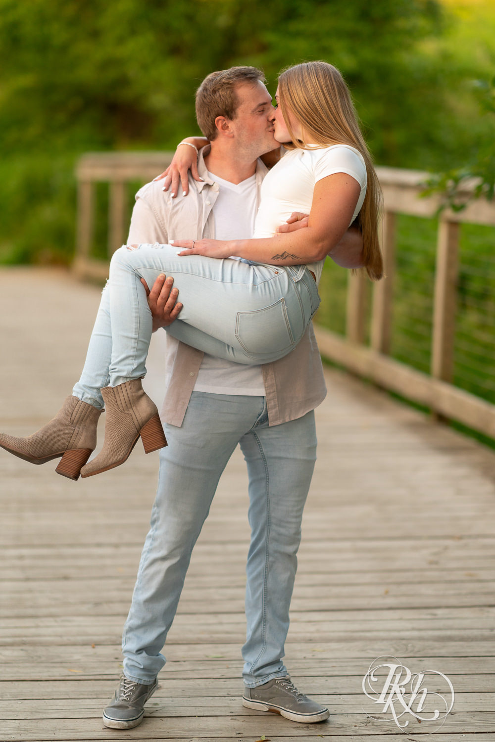 Man and woman in jeans kiss on bridge during golden hour engagement photography in Eagan, Minnesota.