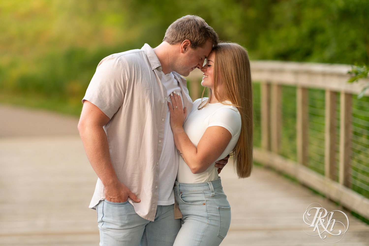 Man and woman in jeans smile on bridge during golden hour engagement photography in Eagan, Minnesota.