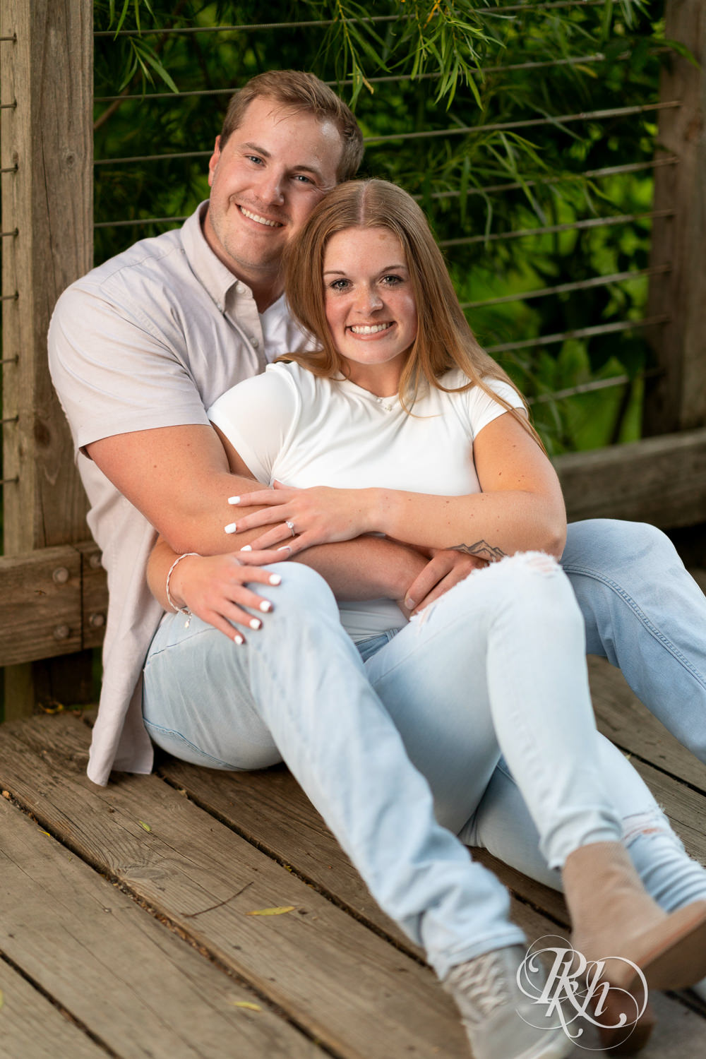 Man and woman in jeans smile on bridge during golden hour engagement photography in Eagan, Minnesota.