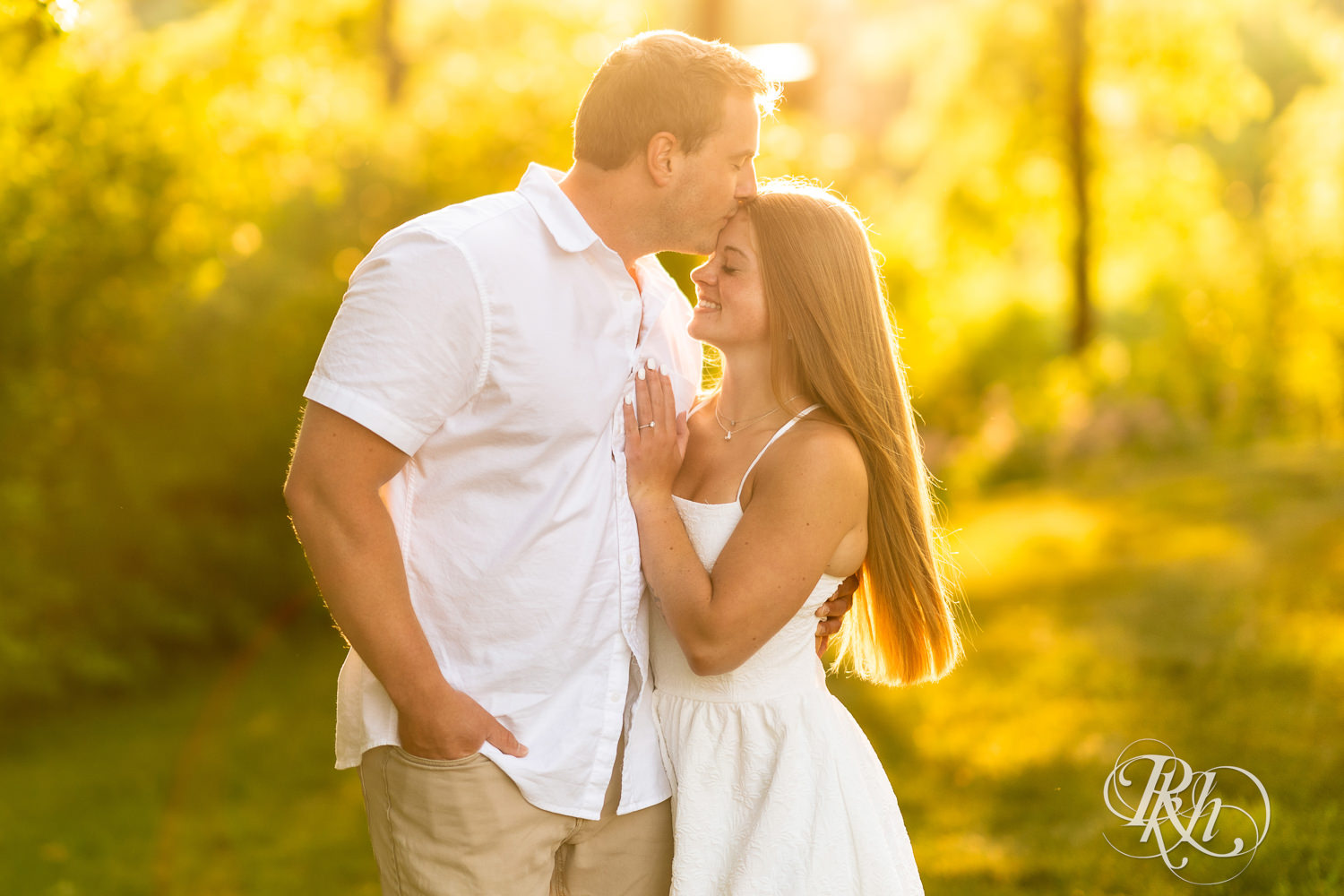 Man in white shirt and woman in white dress smile during golden hour engagement photography at Lebanon Hills in Eagan, Minnesota.