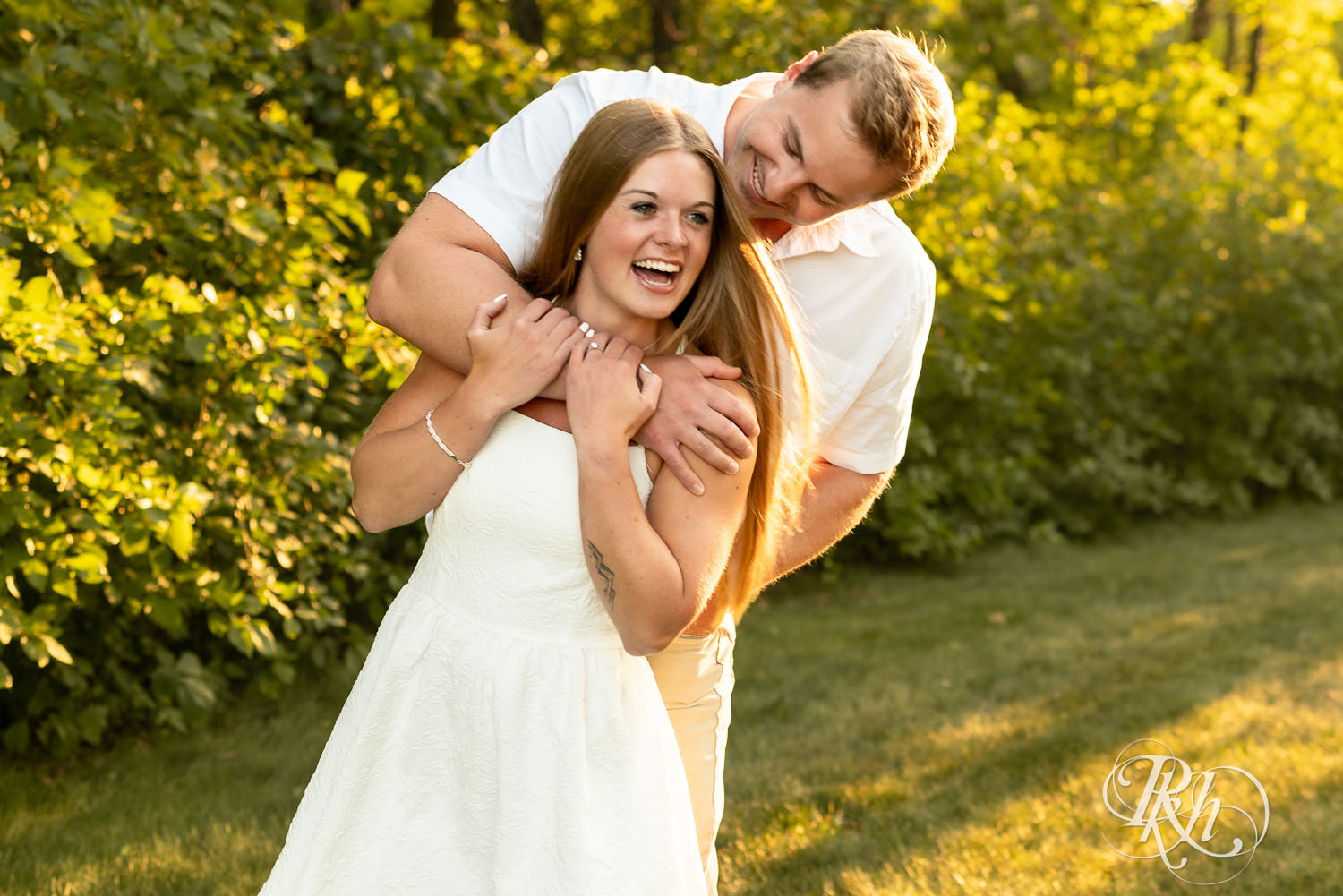 Man in white shirt and woman in white dress laugh during golden hour engagement photography at Lebanon Hills in Eagan, Minnesota.