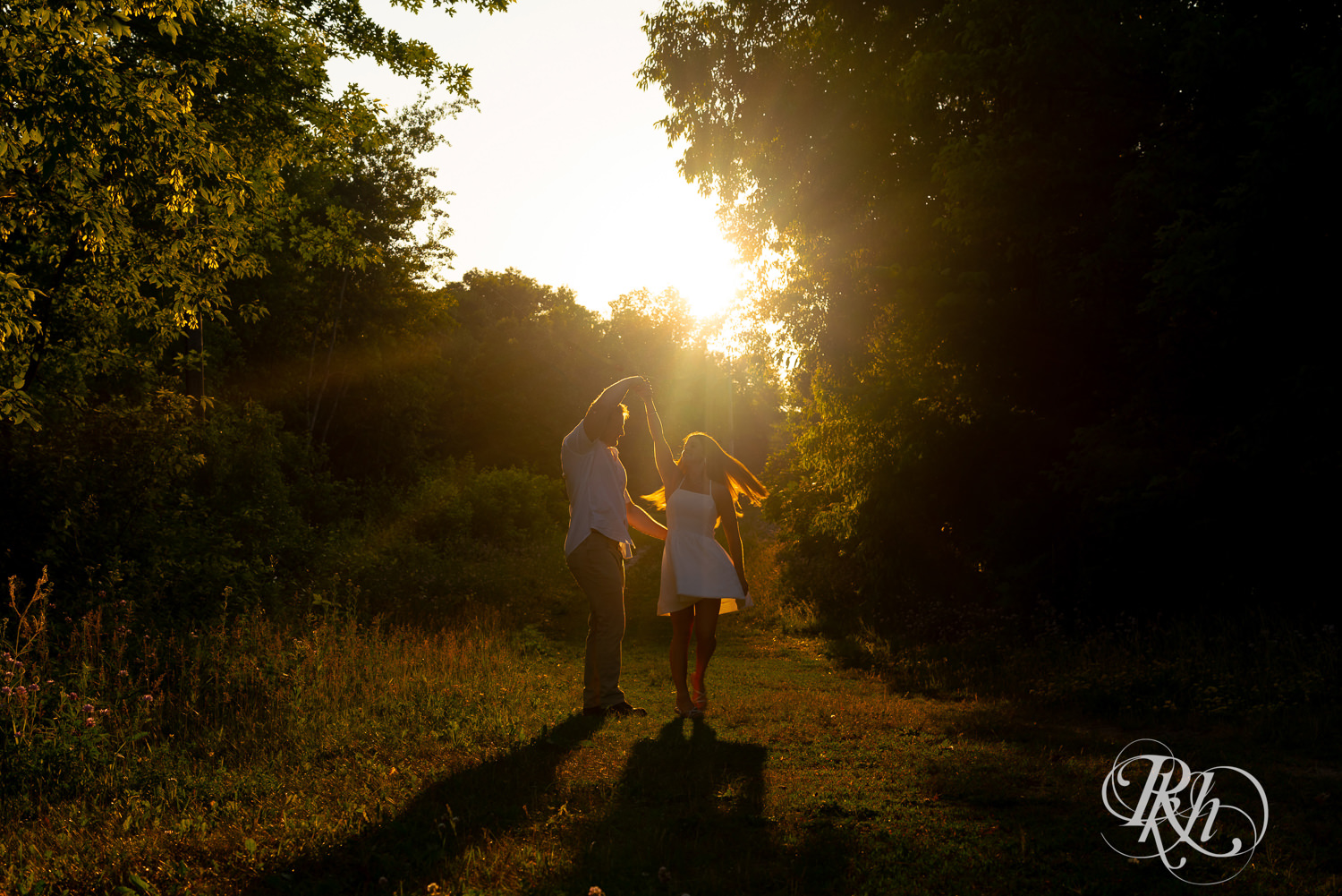 Man in white shirt and woman in white dress dance during golden hour engagement photography at Lebanon Hills in Eagan, Minnesota.