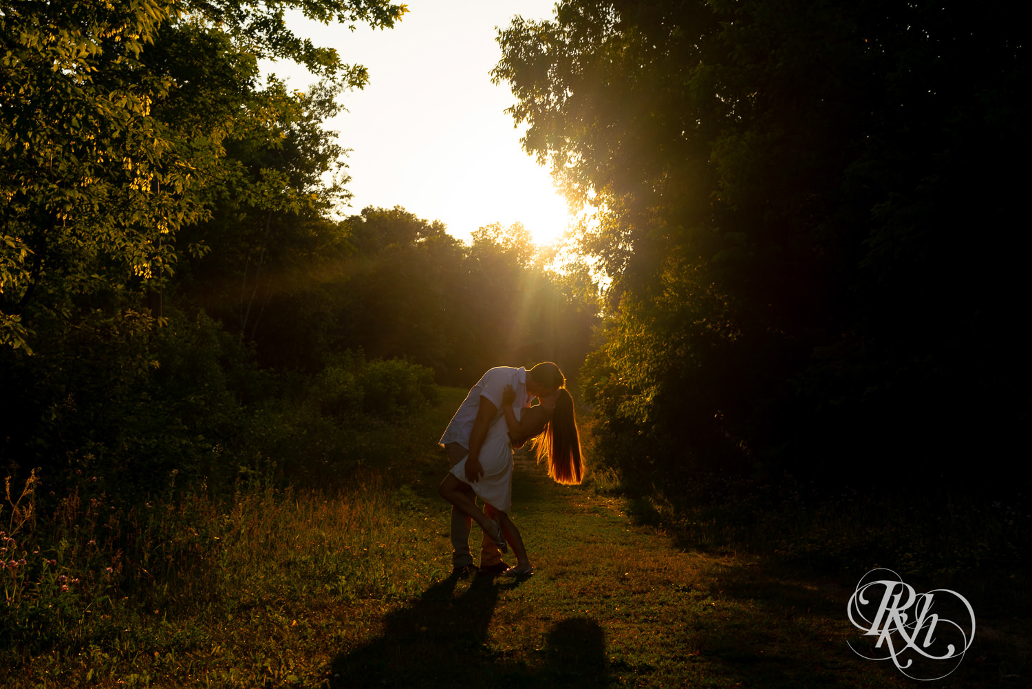 Man in white shirt and woman in white dress kiss during golden hour engagement photography at Lebanon Hills in Eagan, Minnesota.