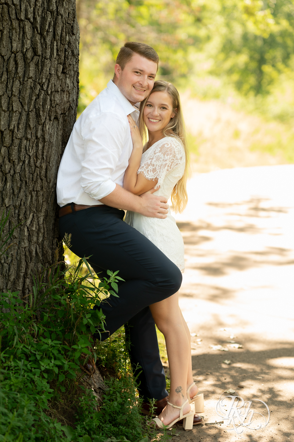 Man and woman dressed in white smile during summer engagement photography in Minnesota.