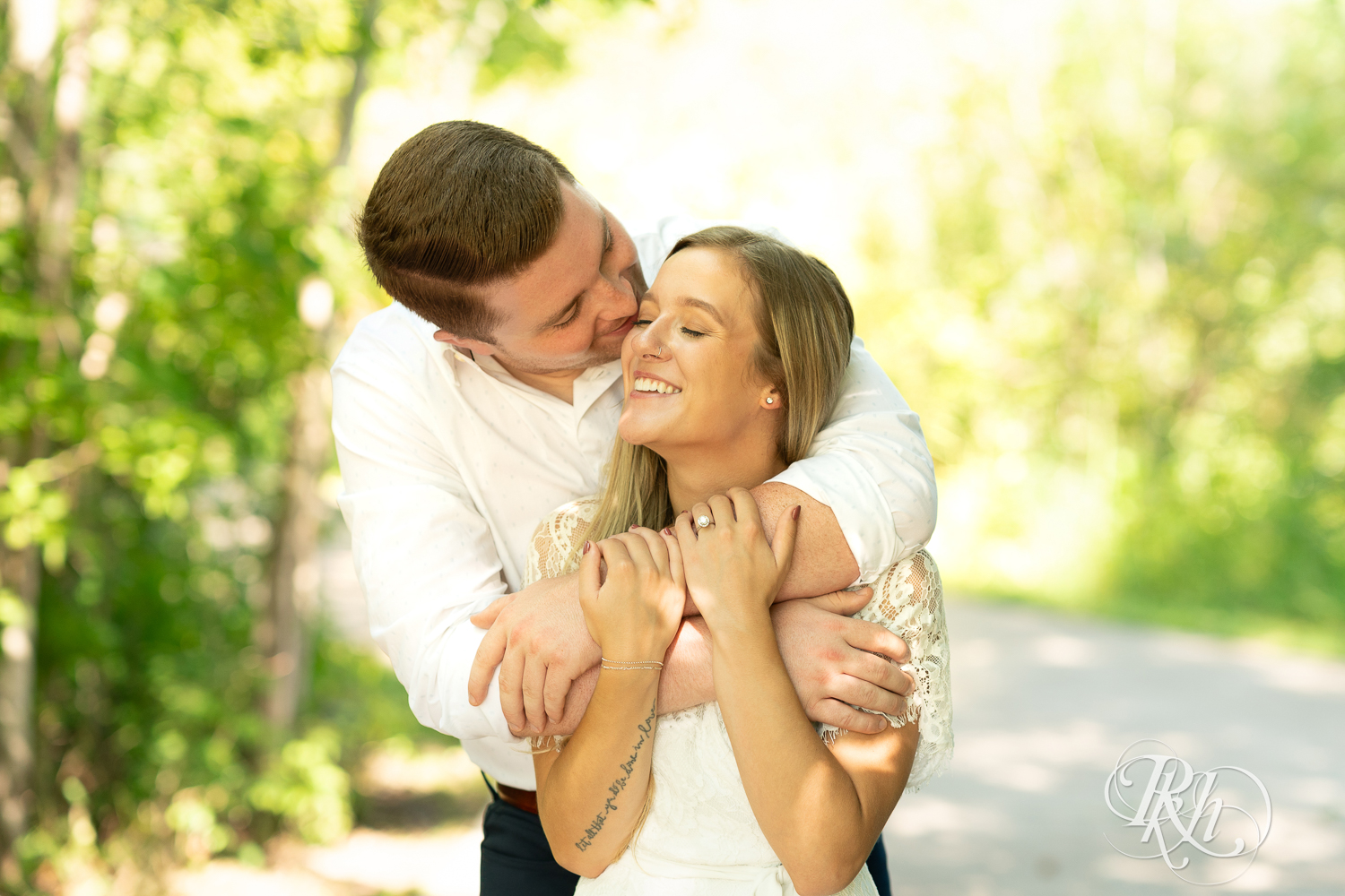 Man and woman dressed in white smile during summer engagement photography in Minnesota.