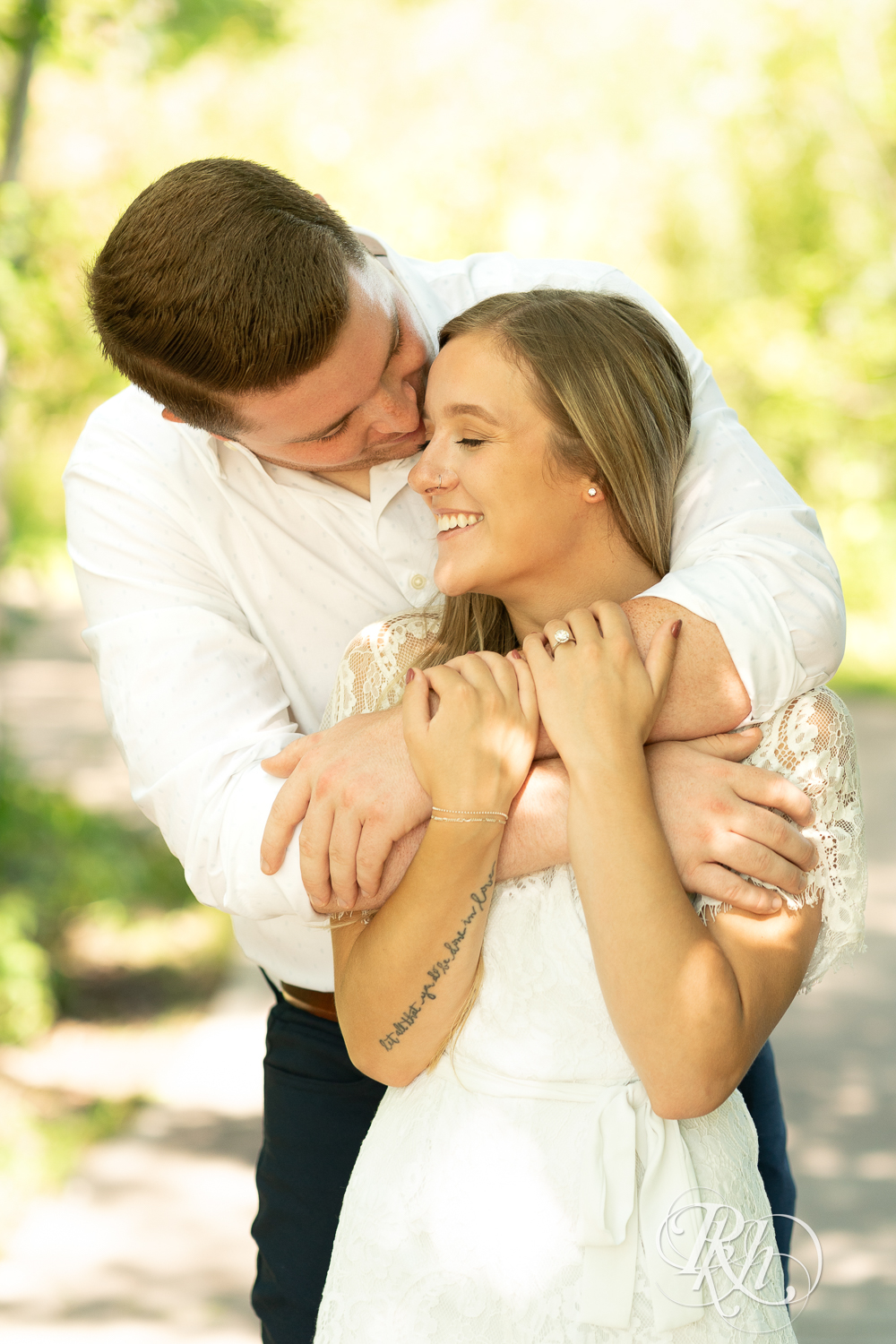 Man and woman dressed in white snuggle during summer engagement photography in Minnesota.