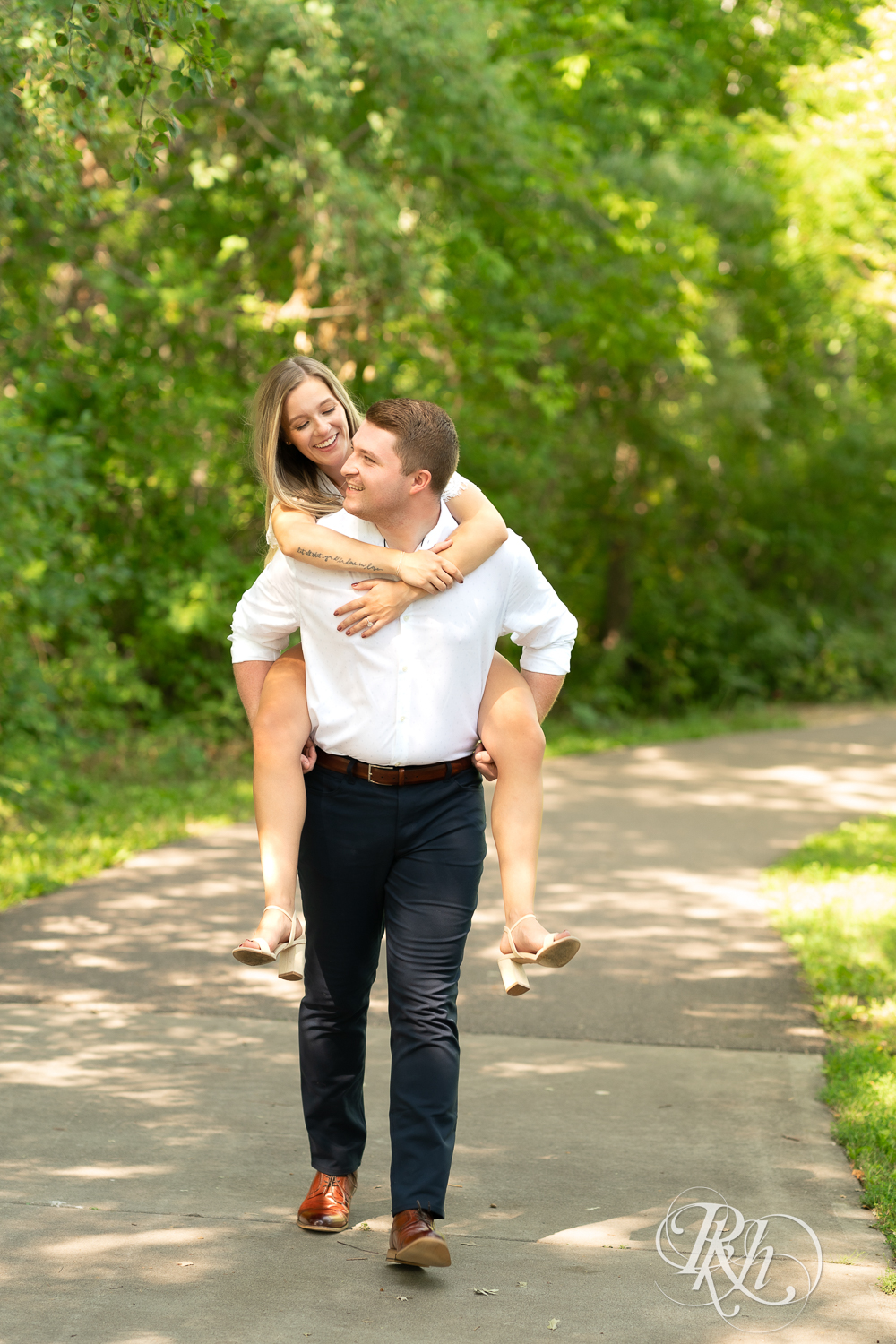Man gives woman a piggyback ride during summer engagement photography in Minnesota.