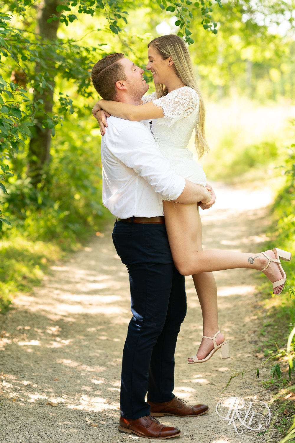 Man lifts woman during summer engagement photography in Minnesota.