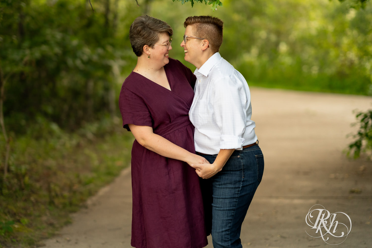 Lesbian couple smile and kiss during engagement photos at Lebanon Hills Regional Park in Eagan, Minnesota.