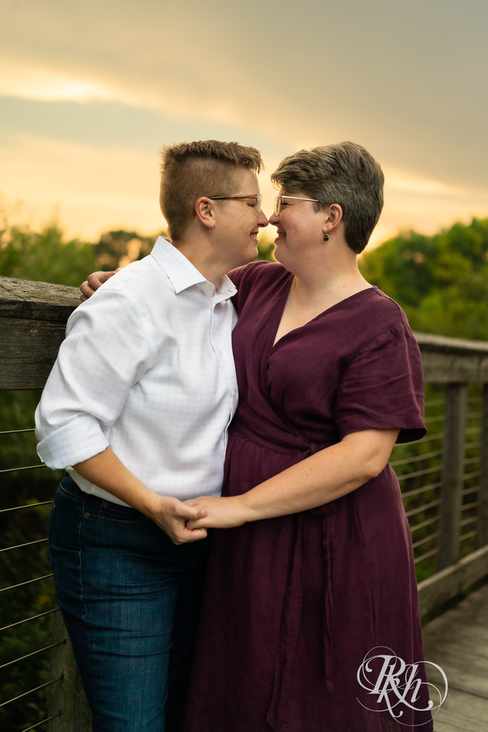 Lesbian couple kiss on bridge during sunset engagement photos at Lebanon Hills Regional Park in Eagan, Minnesota.