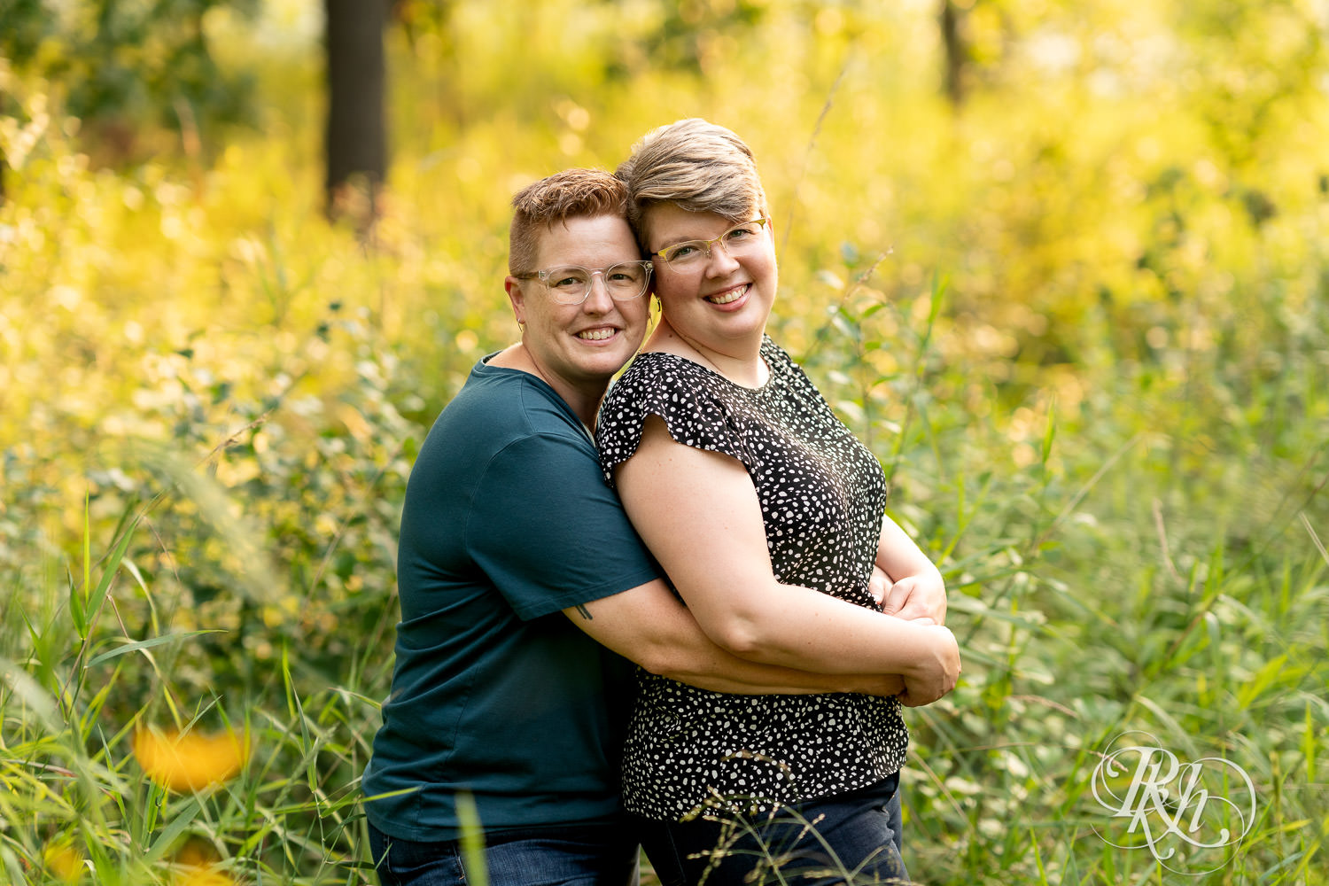 Lesbian couple smile and kiss during engagement photos at Lebanon Hills Regional Park in Eagan, Minnesota.