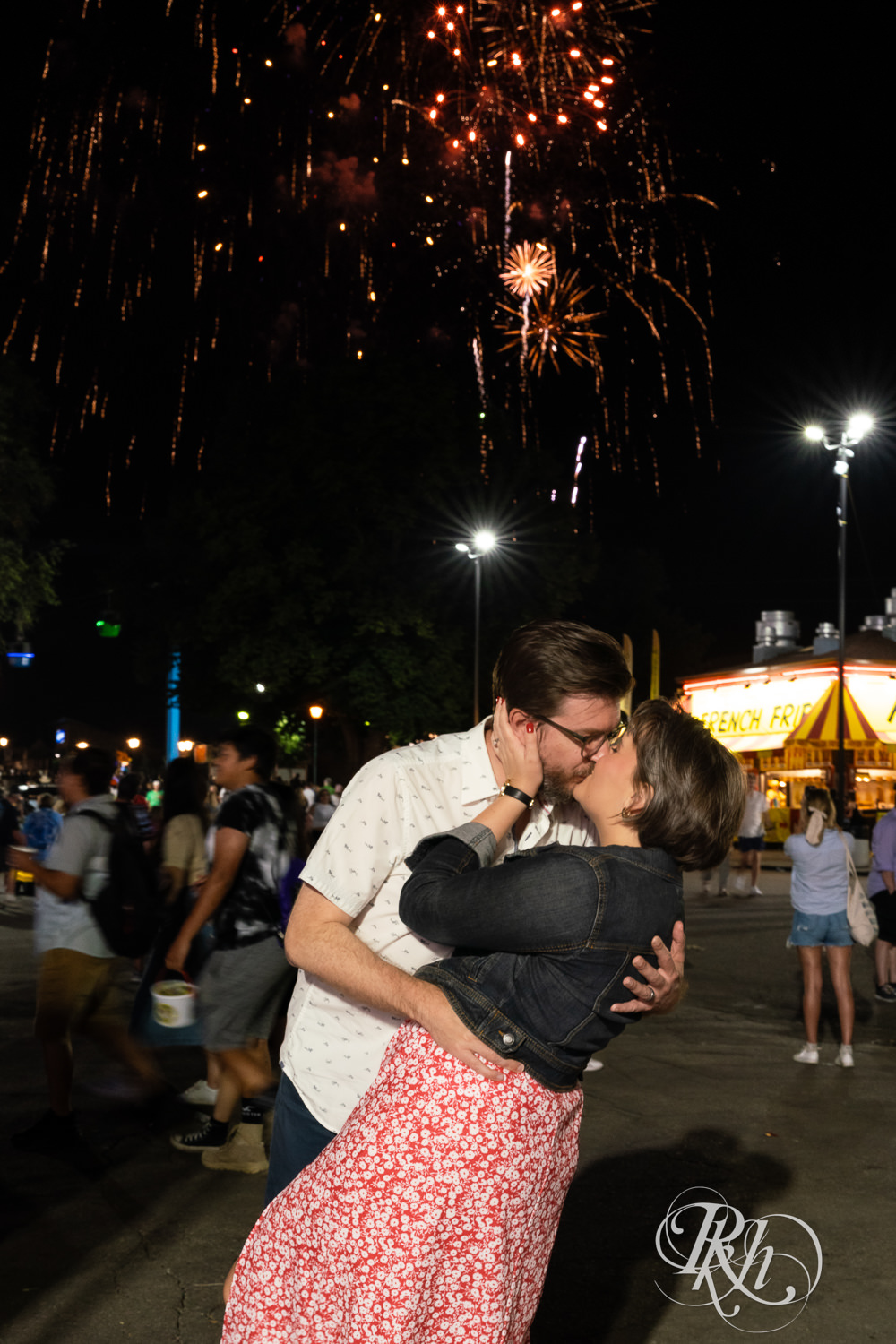 Man and woman kiss under fireworks during their engagement photography at the Minnesota State Fair. 