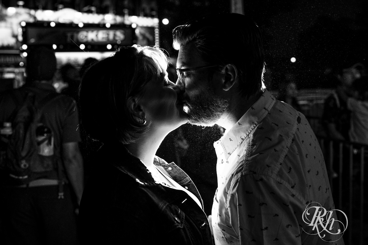 Man and woman kiss at night during their engagement photography at the Minnesota State Fair. 