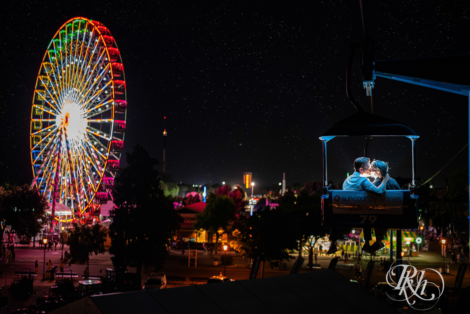 Man and woman kiss on Sky Glider at night during their engagement photography at the Minnesota State Fair. 