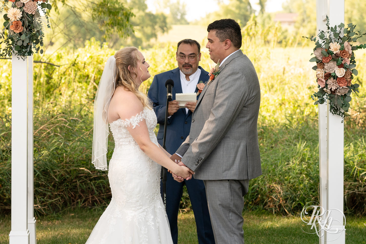 Bride and groom hold hands during summer wedding ceremony at Cottage Farmhouse in Glencoe, Minnesota.