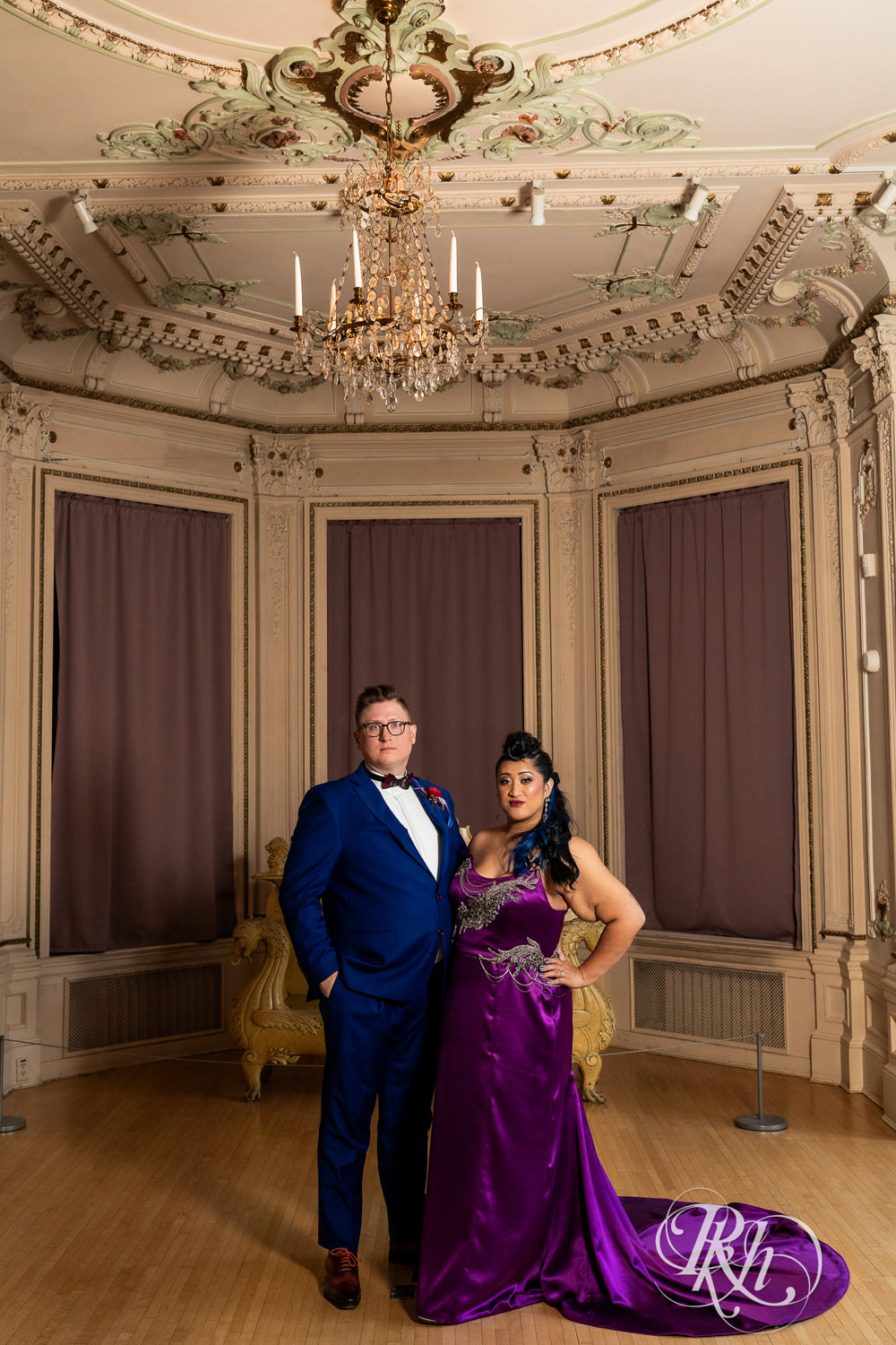 Filipino bride with mohawk dressed in purple wedding and groom pose stoic under chandelier  at American Swedish Institute in Minnesota.