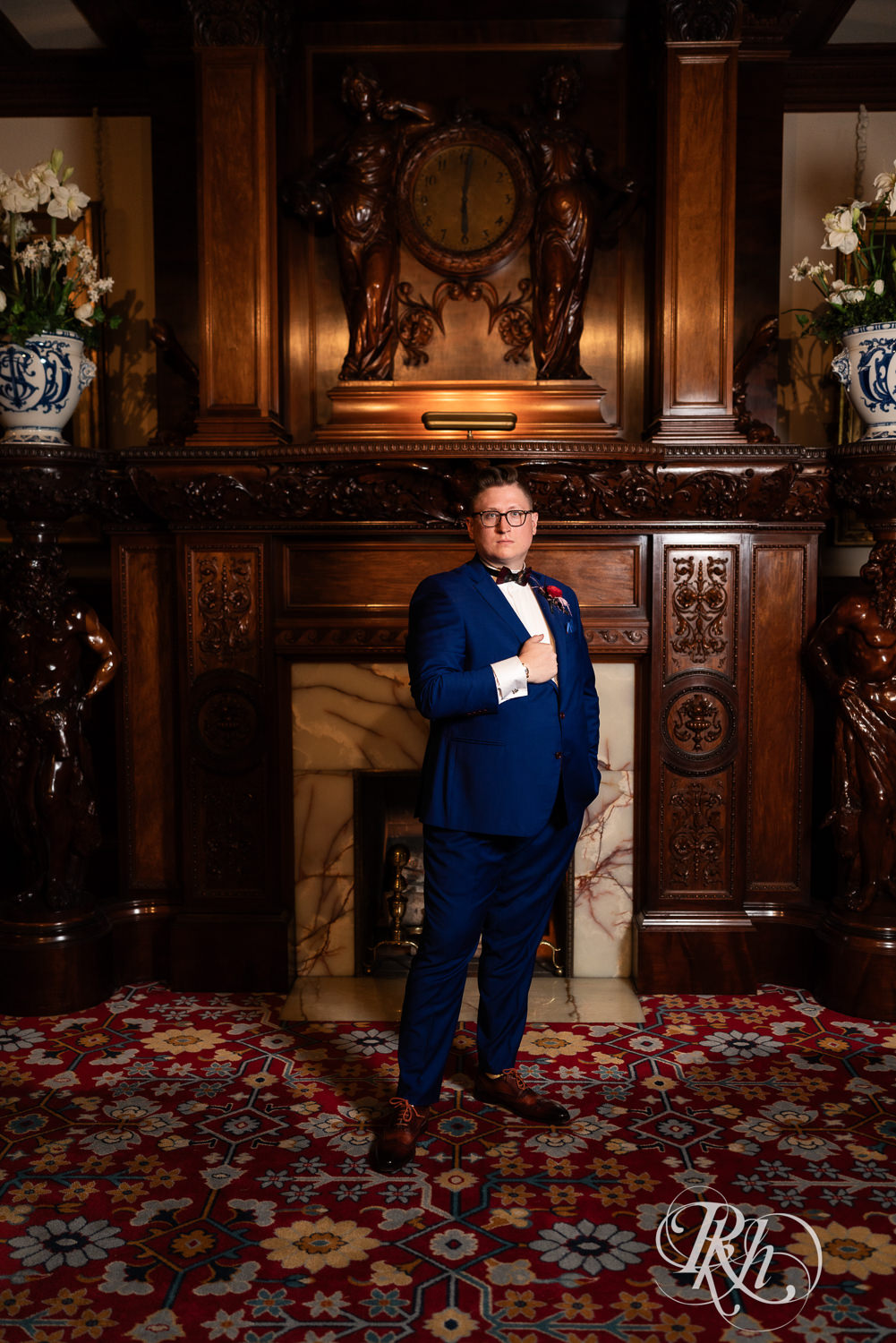 Groom in blue suit stands in front of fireplace at American Swedish Institute in Minnesota.