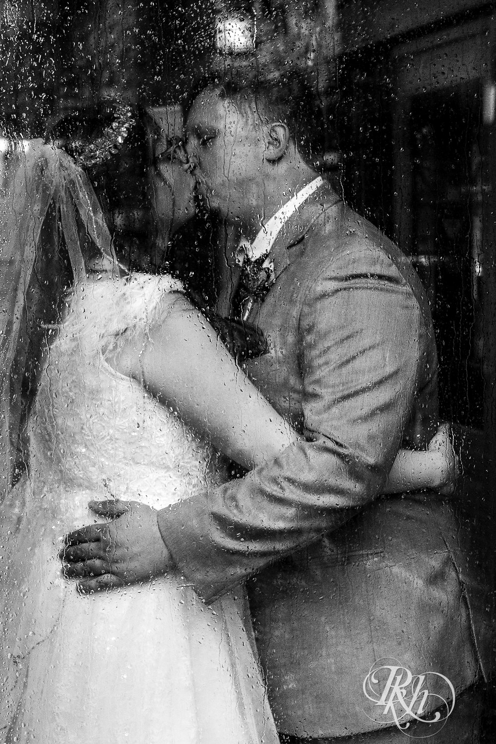 Bride and groom kiss in front of rainy window at Bunker Hills Event Center in Coon Rapids, Minnesota.