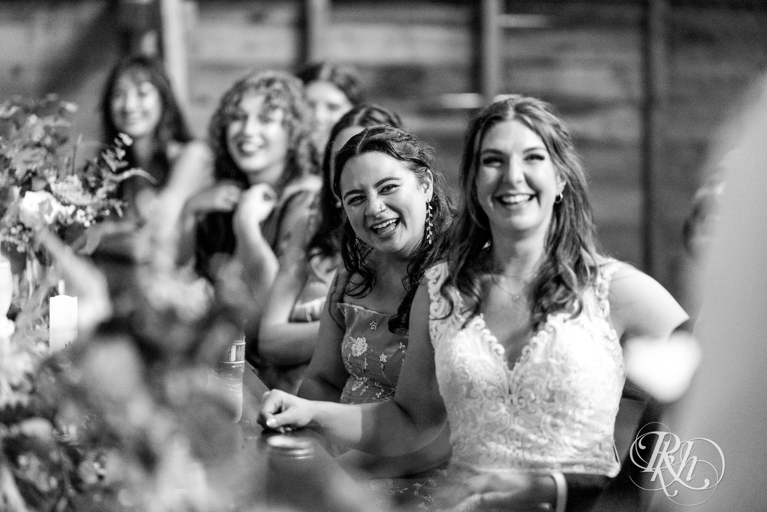 Bride, groom and wedding party smile during speeches at wedding reception at Hayvn at Hay River in Boyceville, Wisconsin. 