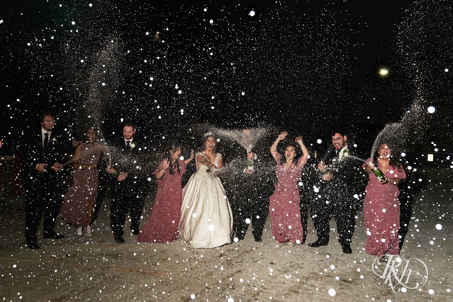 Bride and groom spray champagne in a parking ramp with their wedding party.