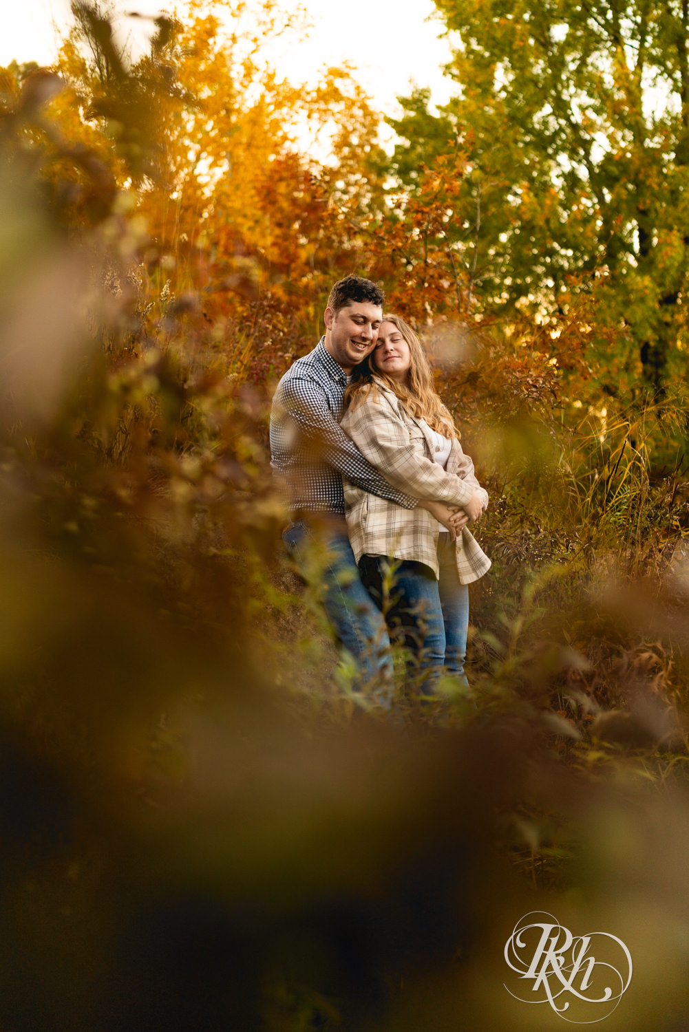 Man and woman in jeans snuggle during fall engagement photos at Lebanon Hills Regional Park in Eagan, Minnesota.