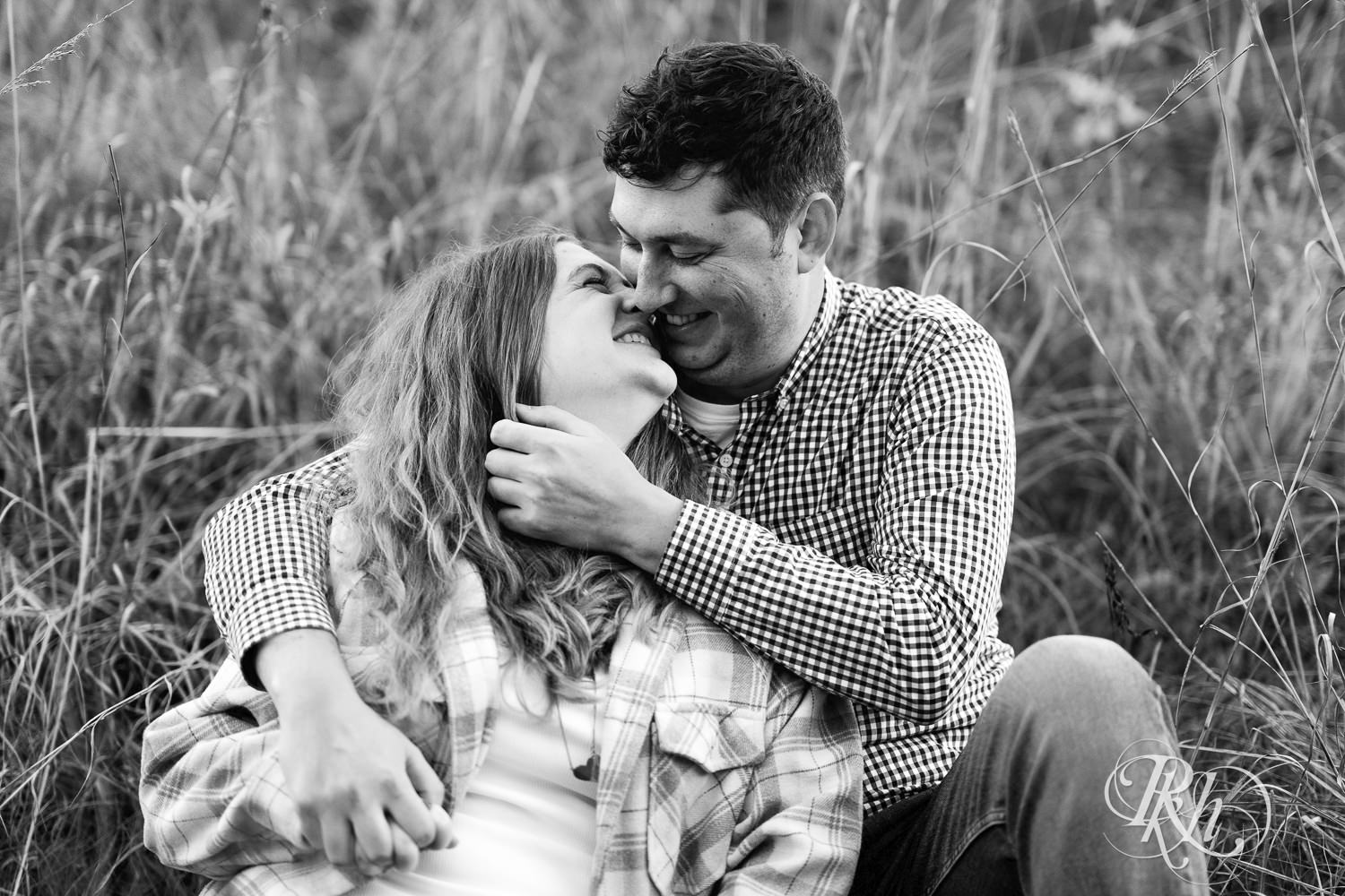 Man and woman in jeans snuggle during fall engagement photos at Lebanon Hills Regional Park in Eagan, Minnesota.