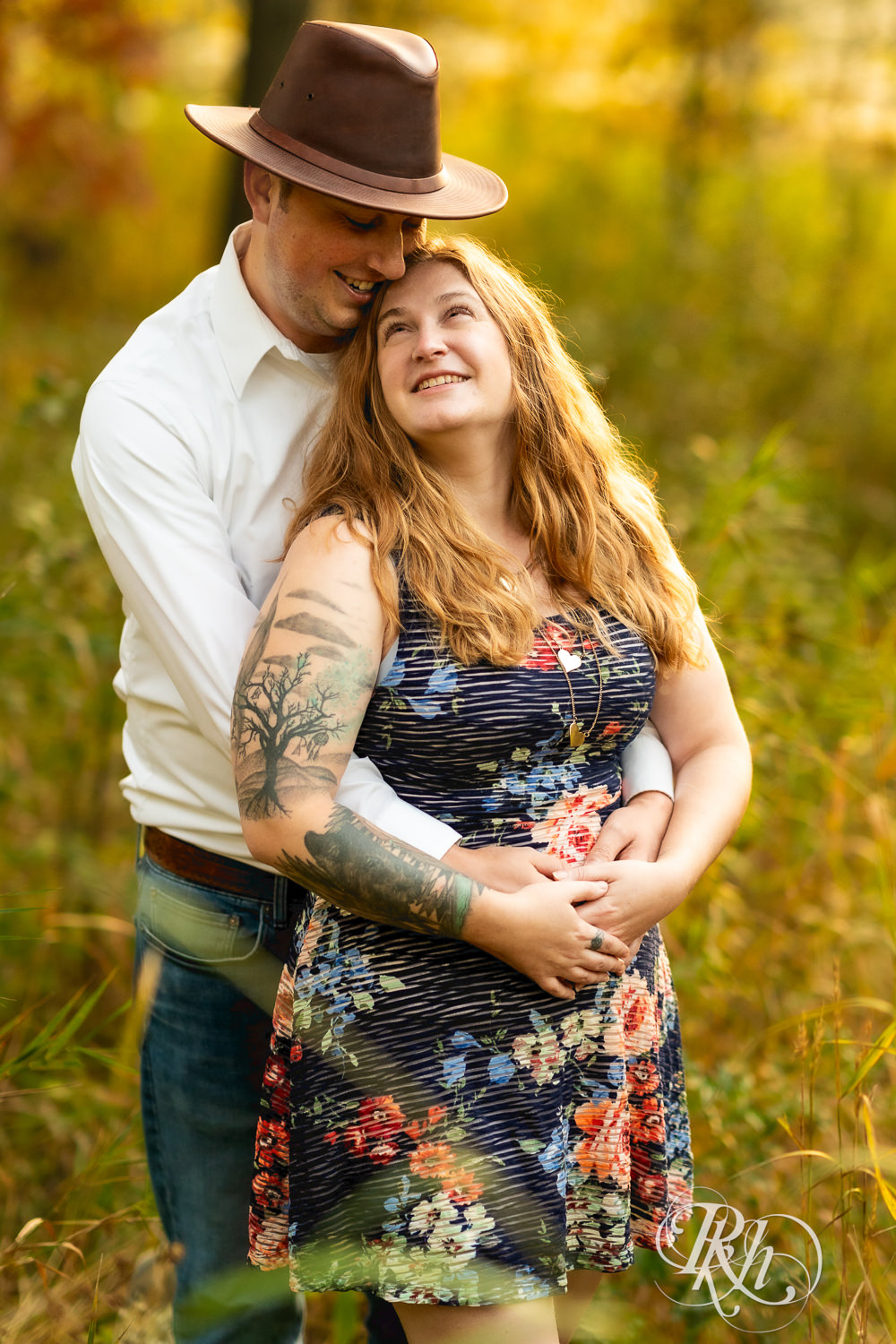 Man in hat and jeans and woman in dress snuggle during fall engagement photos at Lebanon Hills Regional Park in Eagan, Minnesota.