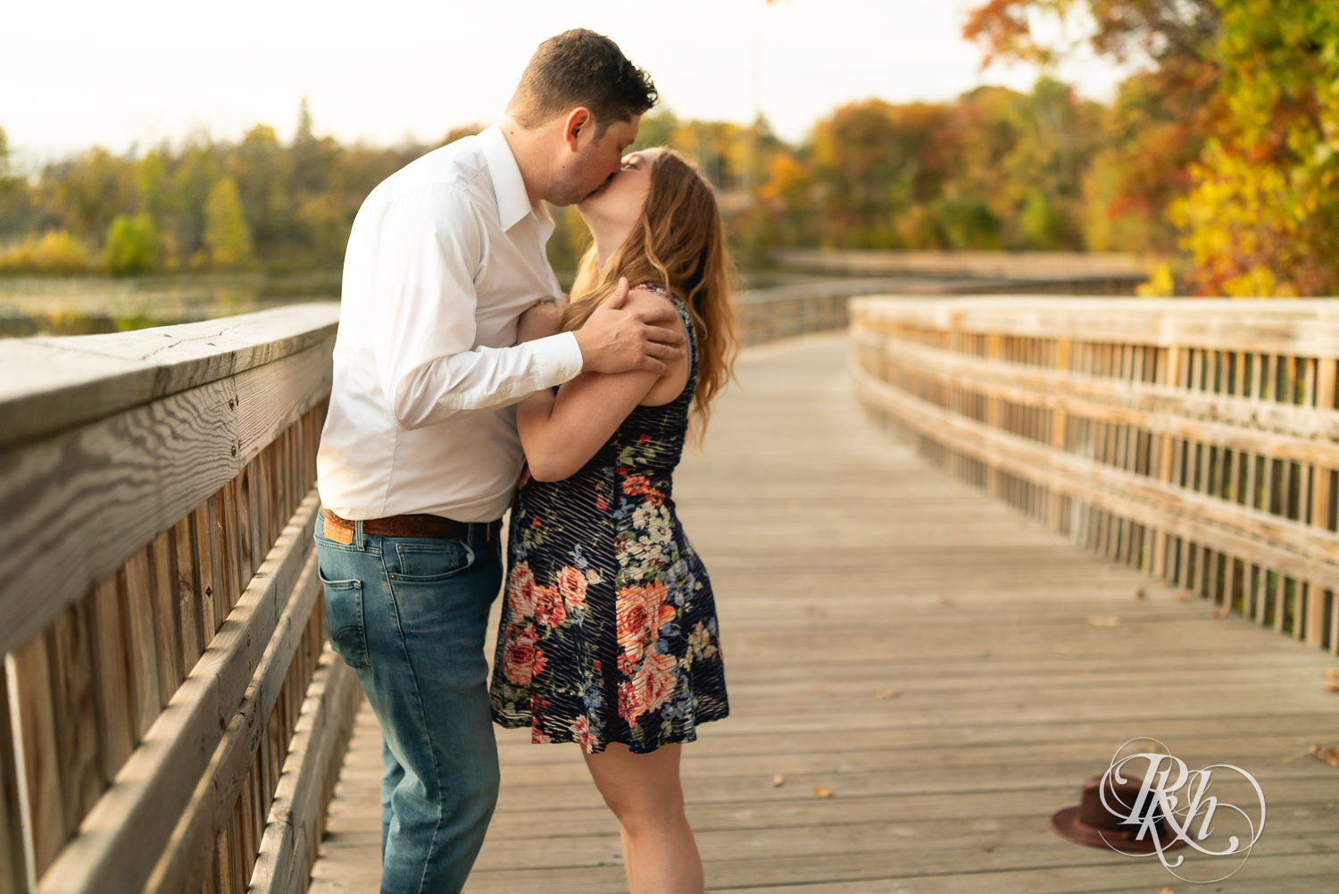 Man in hat and jeans and woman in dress kiss on bridge at Lebanon Hills Regional Park in Eagan, Minnesota.