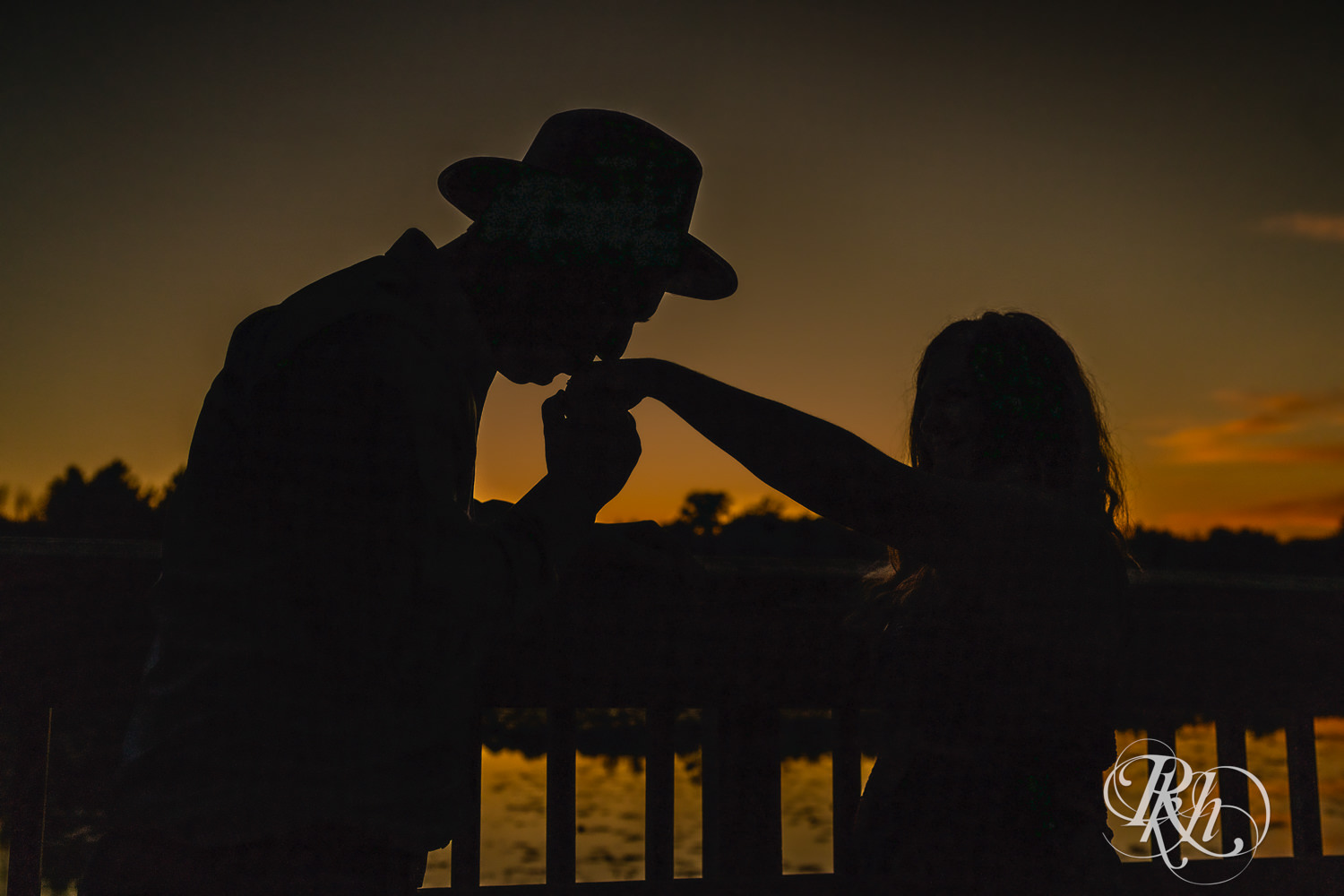 Man in hat and jeans and woman in dress kiss in silhouette at Lebanon Hills Regional Park in Eagan, Minnesota.