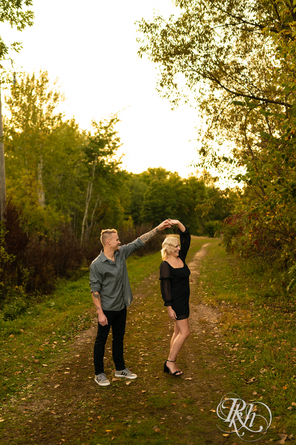 Blond woman in black dress and man in dress shirt damce during sunset engagement photos at Lebanon Hills Regional Park in Eagan, Minnesota.