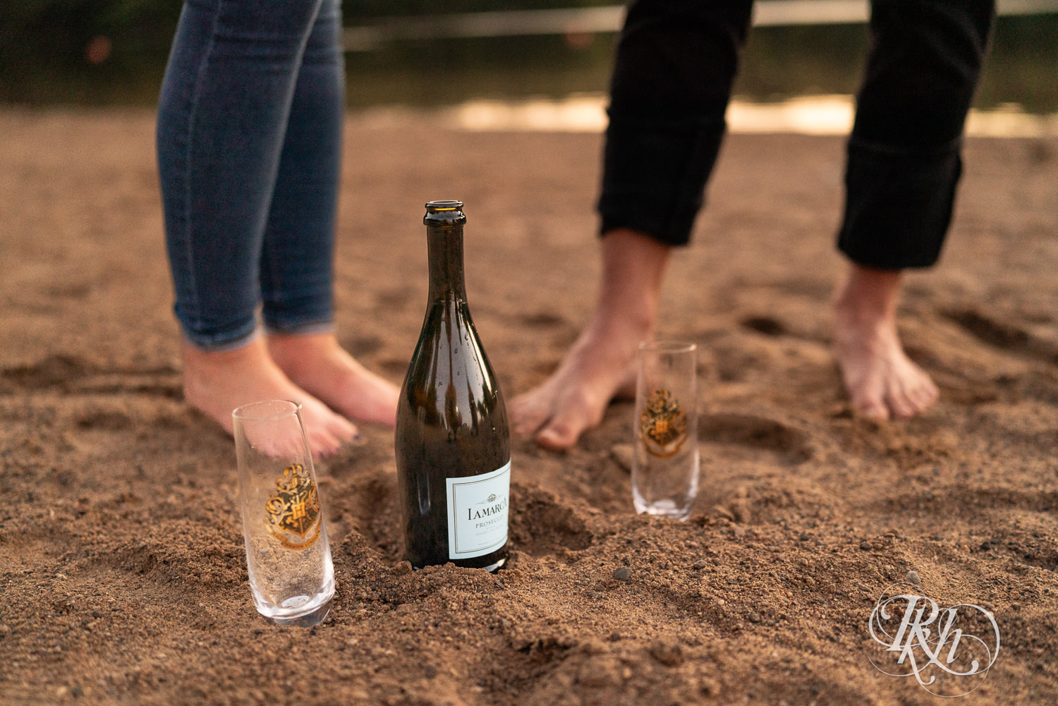 Blond woman and man in white shirts and jeans drink champagne on the beach at Lebanon Hills Regional Park in Eagan, Minnesota.