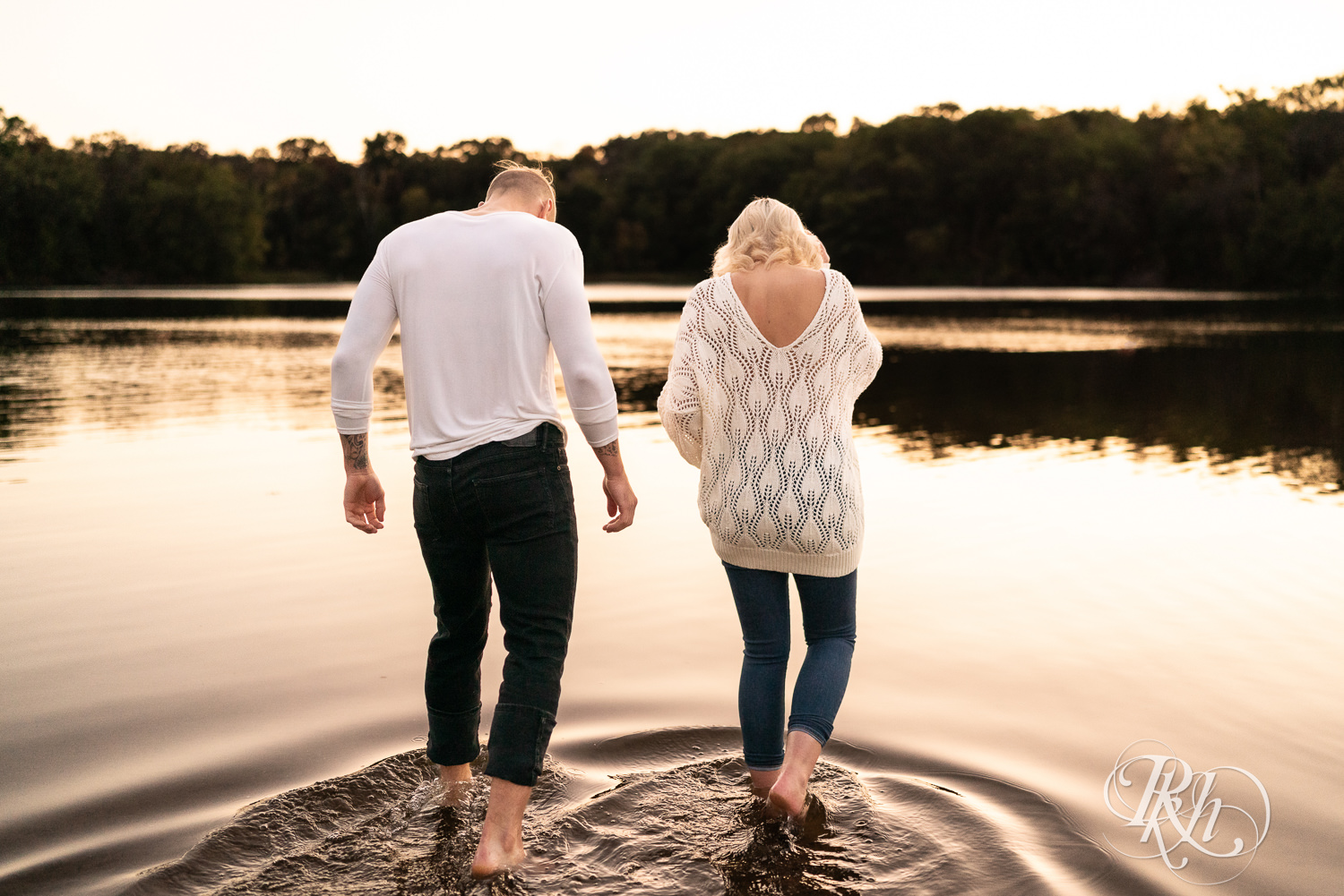 Blond woman and man in white shirts and jeans walk in the lake at Lebanon Hills Regional Park in Eagan, Minnesota.