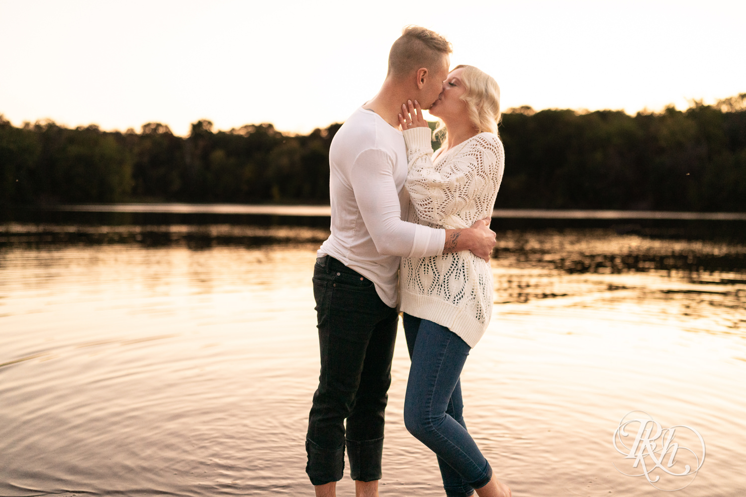 Blond woman and man in white shirts and jeans kiss in the lake at Lebanon Hills Regional Park in Eagan, Minnesota.