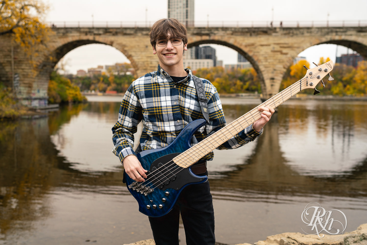 Senior boy smiles during downtown Minneapolis senior photography with cat and bass guitar.