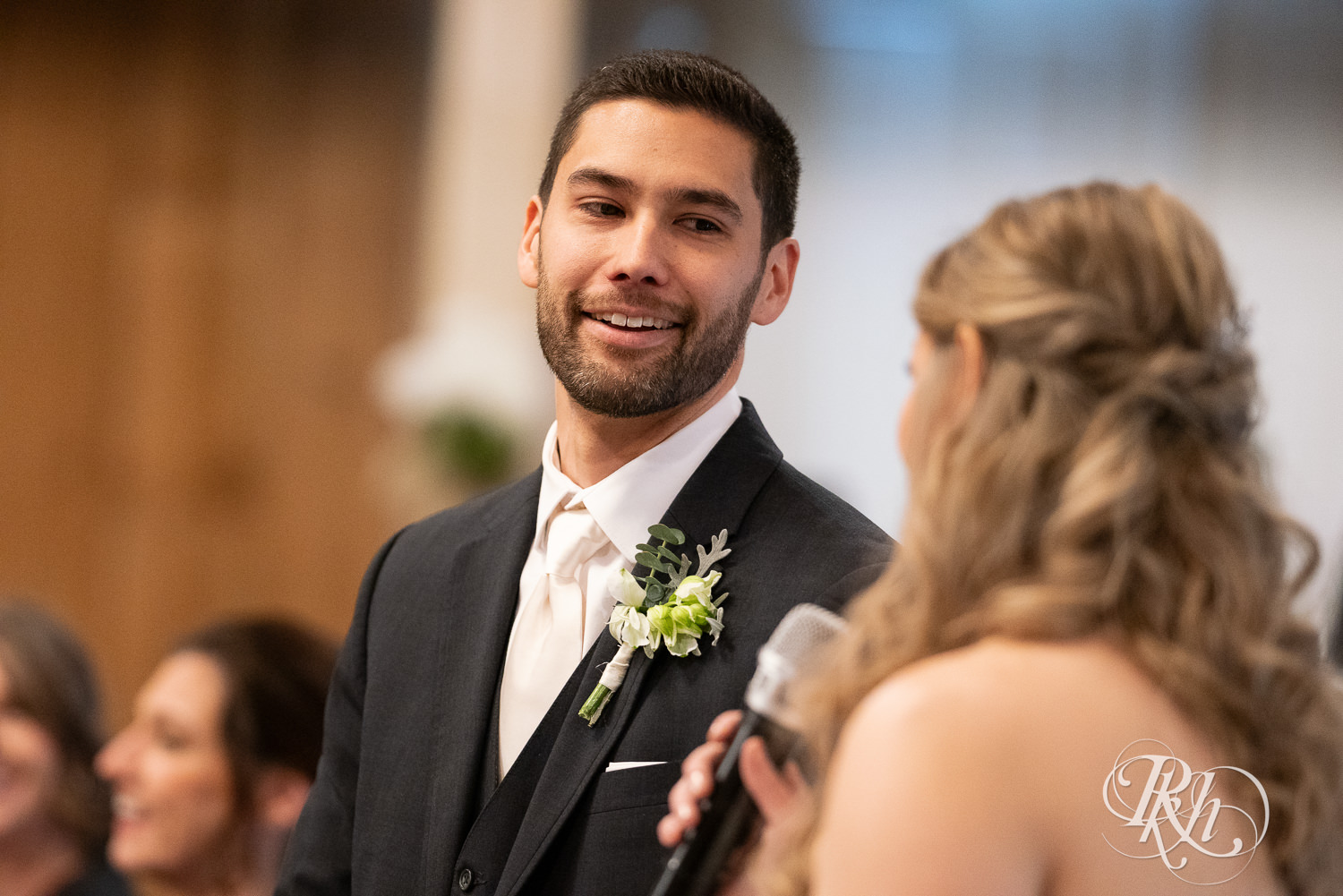 Bride and groom smile during speeches at wedding reception at Almquist Farm in Hastings, Minnesota.