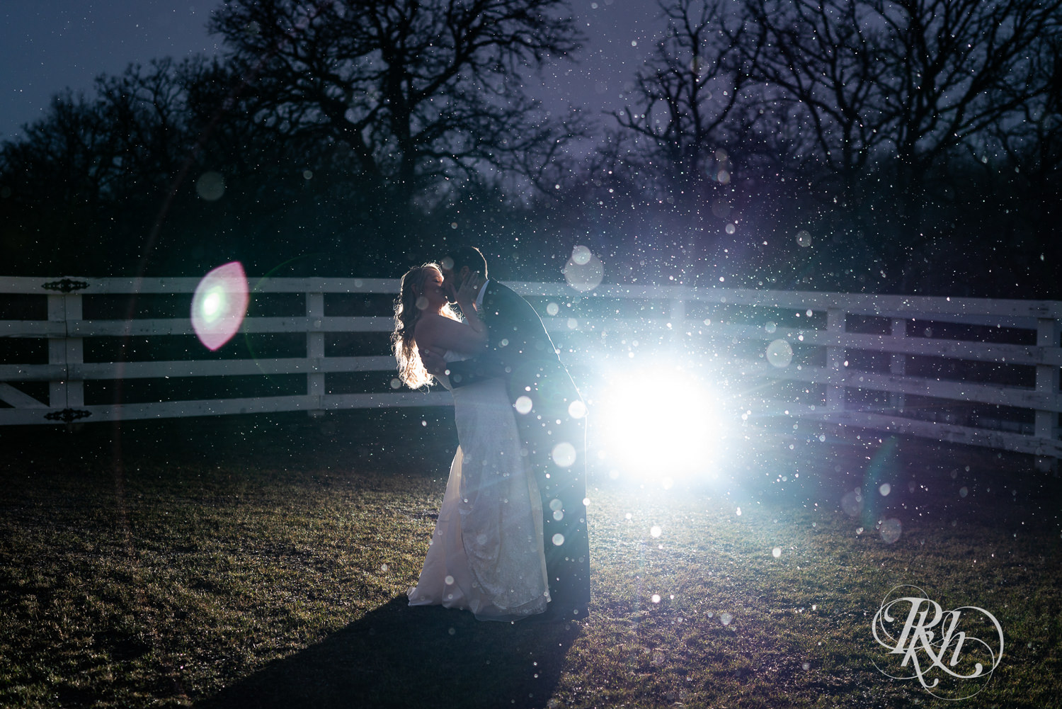 Bride and groom kiss at night in the falling snow at winter wedding at Almquist Farm in Hastings, Minnesota.