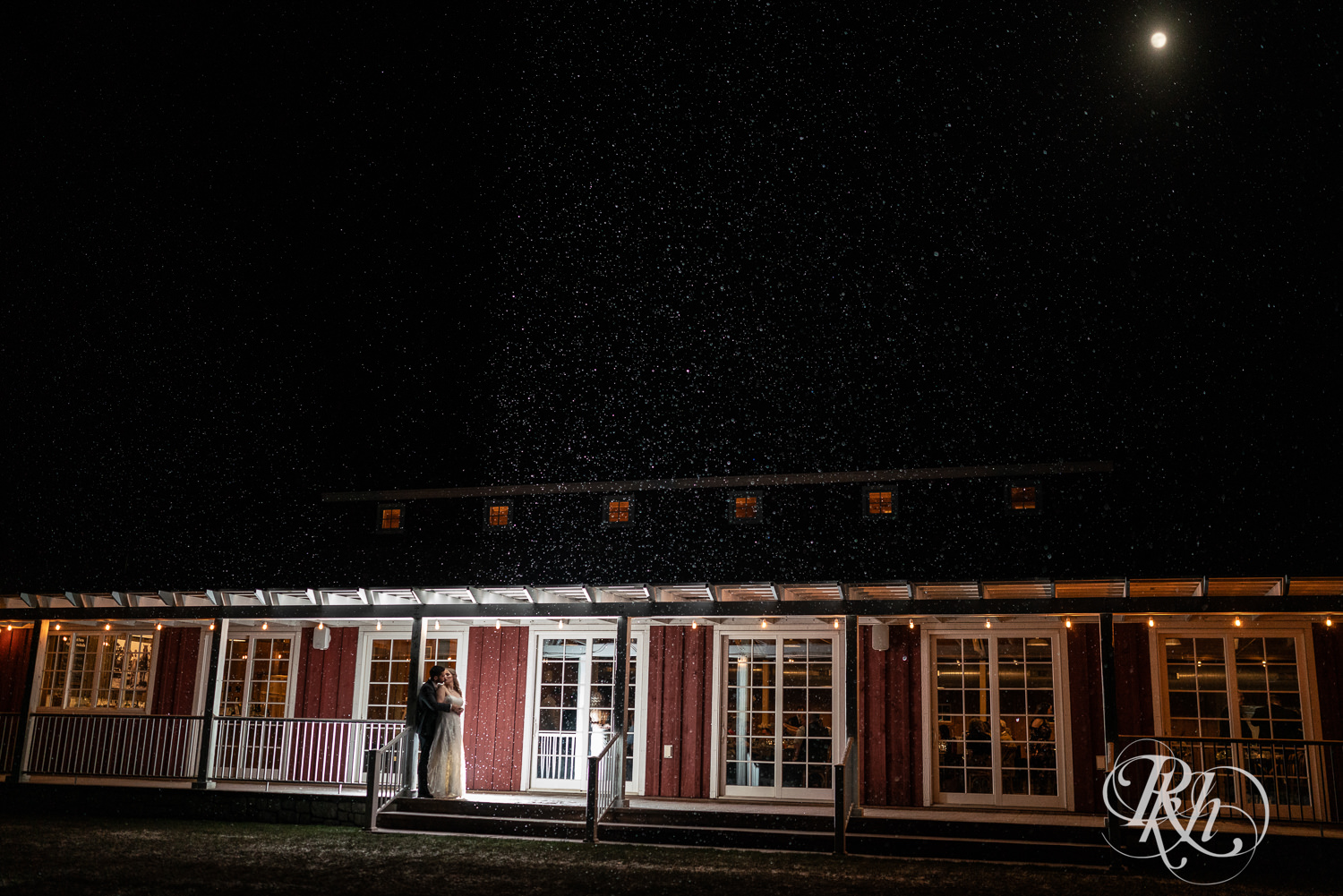 Bride and groom kiss at night in the falling snow at winter wedding at Almquist Farm in Hastings, Minnesota.