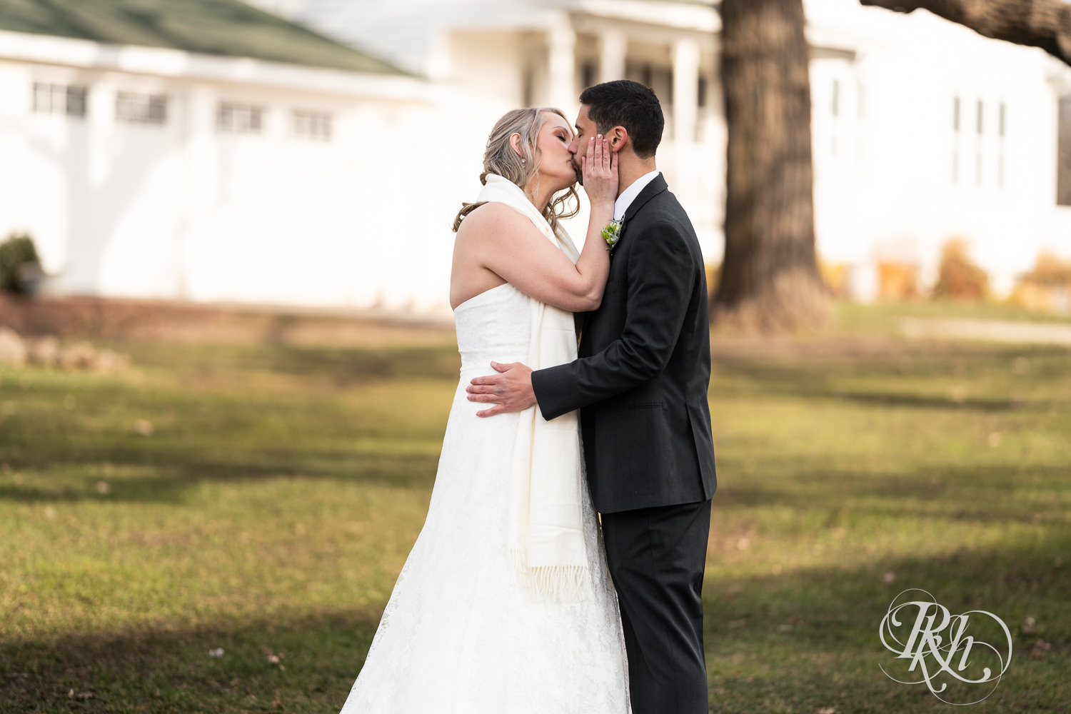 Bride and groom dance and kiss in front of a white farmhouse at Almquist Farm in Hastings, Minnesota.